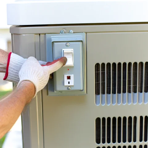 A homeowner safely turning off the power to their air conditioning unit by flipping the switch in the exterior shut-off box, located near the unit
