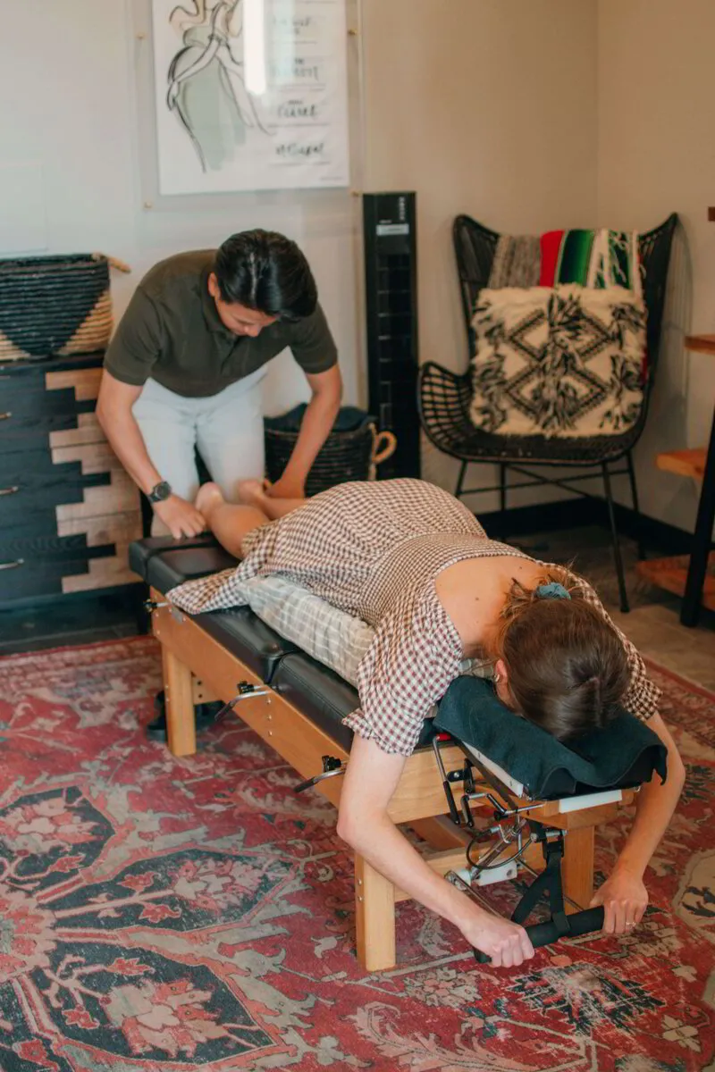Focused chiropractic adjustment by Dr. Binh in a cozy, eclectic clinic setting with a patient resting comfortably on the treatment table
