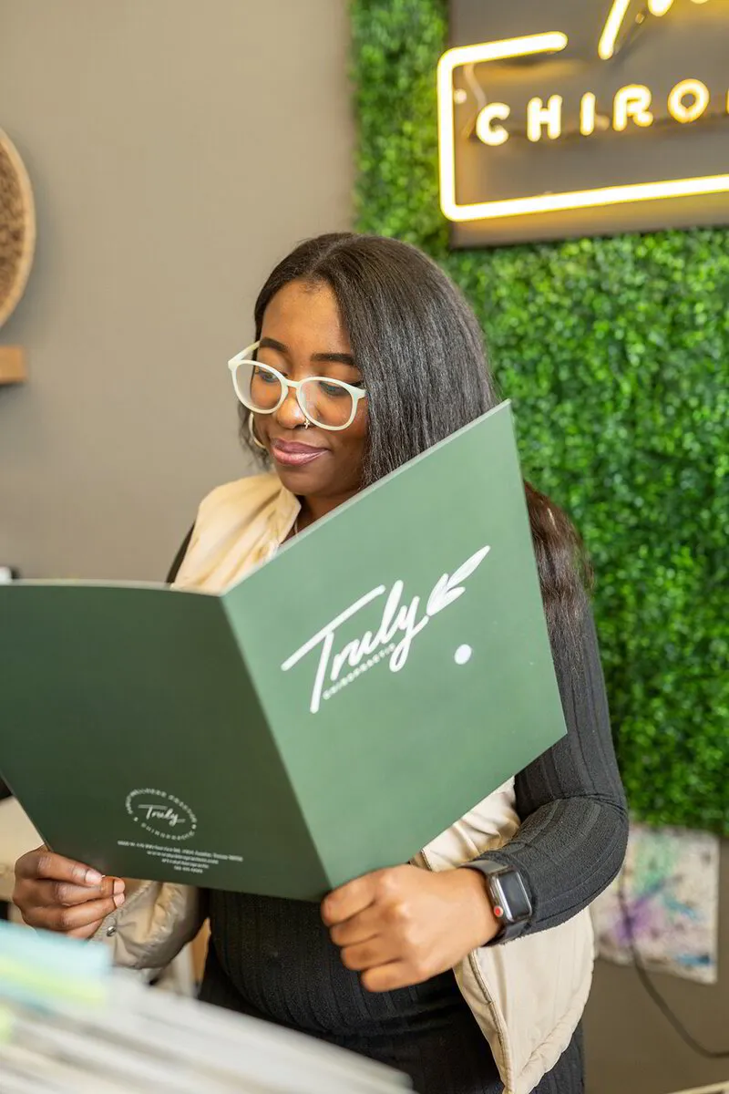 Ariana, a recent graduate passionate about chiropractic care, is absorbed in reading a brochure at Truly Chiropractic's vibrant office.