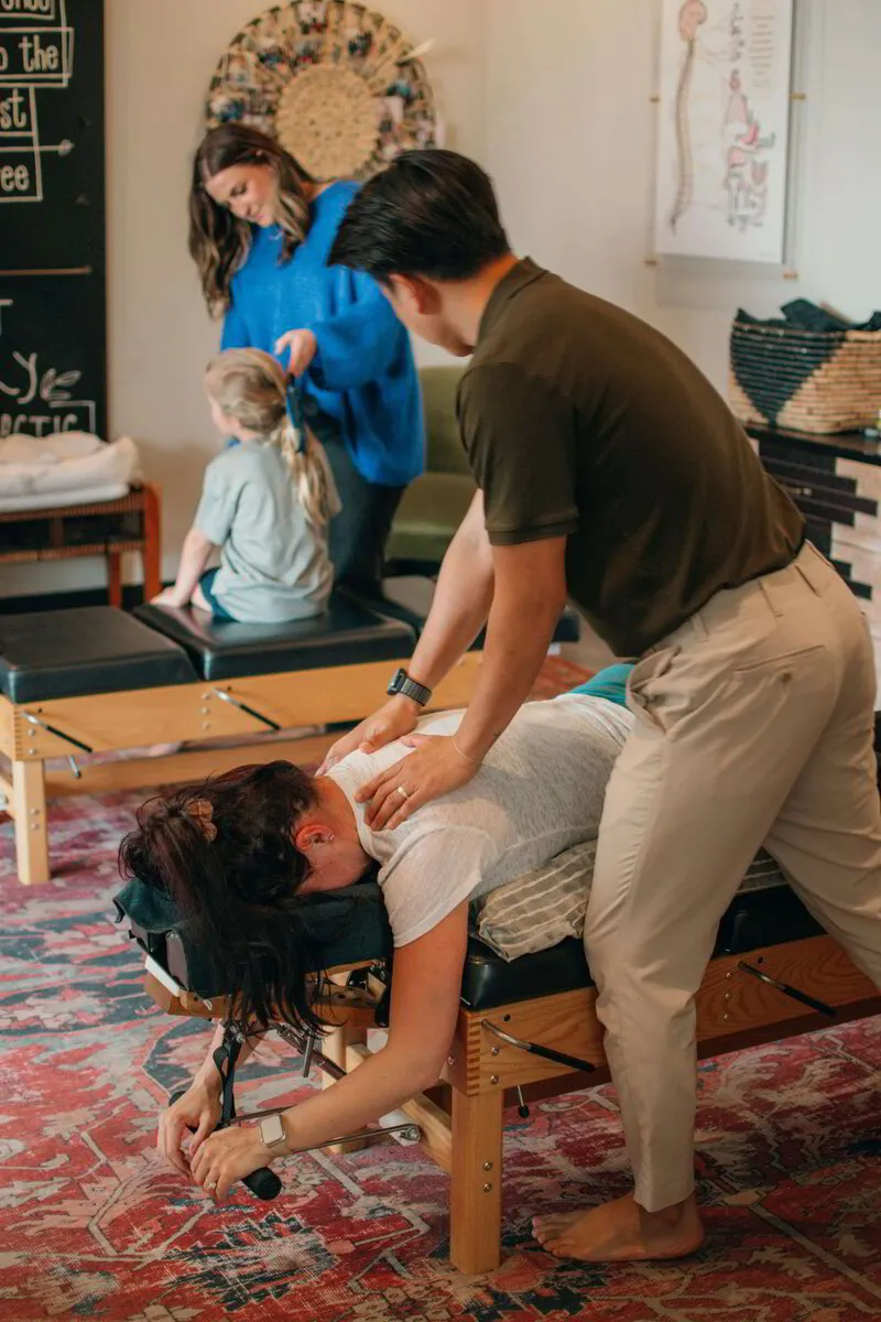 Dr. Binh attentively performs a chiropractic adjustment on a patient, while a colleague and a young visitor engage in the background
