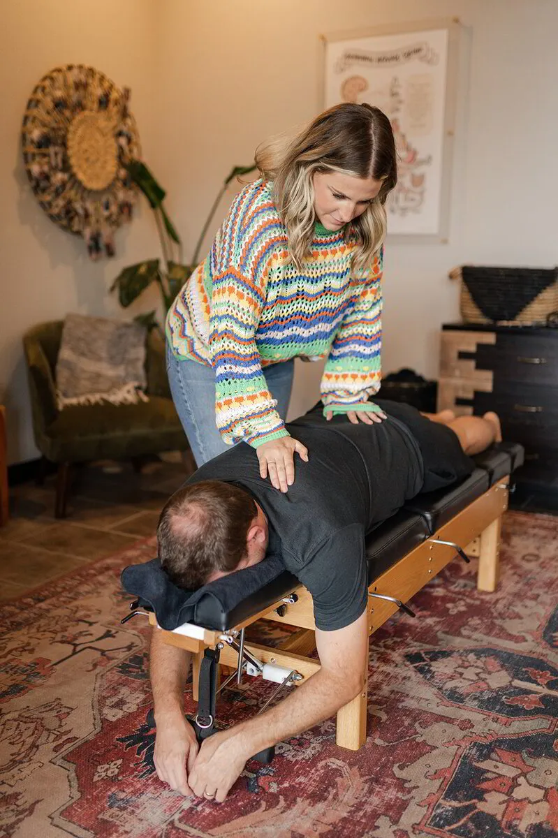 Dr. Morgan, applies pressure to the back of a prone patient on a chiropractic table in a well-decorated clinic room.