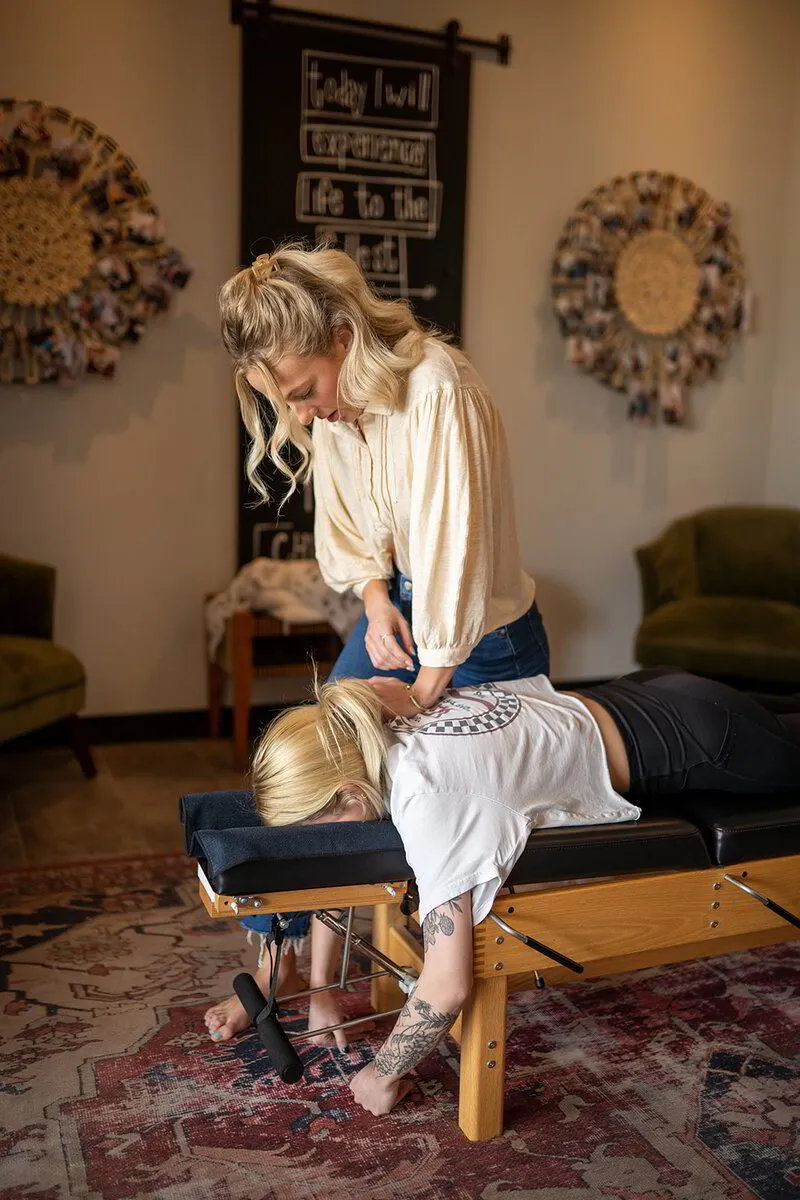Dr. ALEXIS, who is attentively performing an adjustment on a young patient positioned face-down on the chiropractic table.
