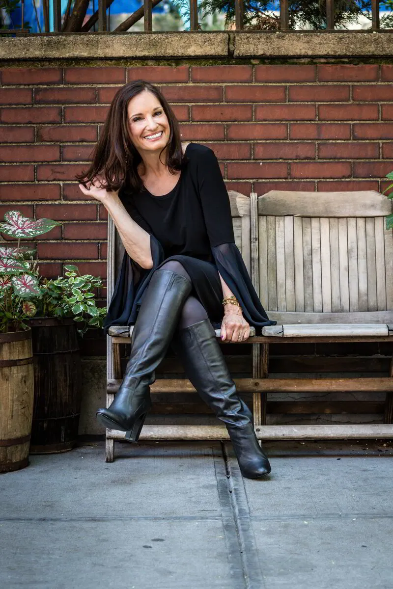 Elise Morris, acclaimed eclectic jazz musician and singer-songwriter, seated gracefully on a rustic wooden bench against a textured brick wall backdrop.