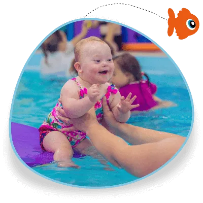 A happy toddler leans off a raft in a swimming pool towards an adult as part of a child swimming lesson