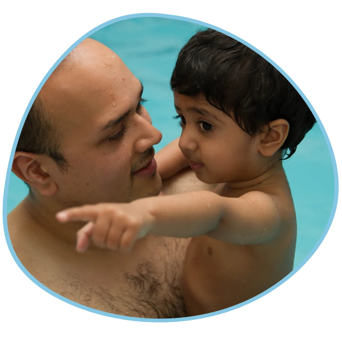 A dad and his child are in a swimming pool and the child is pointing at something