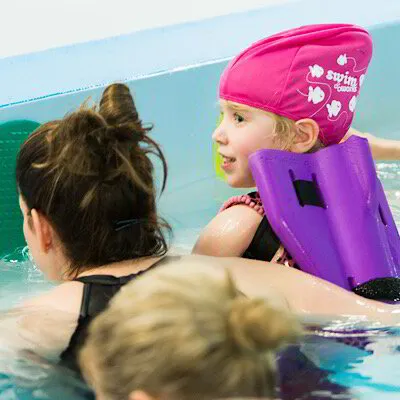 A grown up shows a child how to hold on to the the side of the swimming pool and learn water safety skills