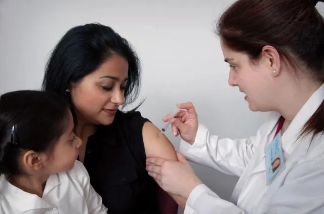 female doctor administering vaccination to mother holding onto young child