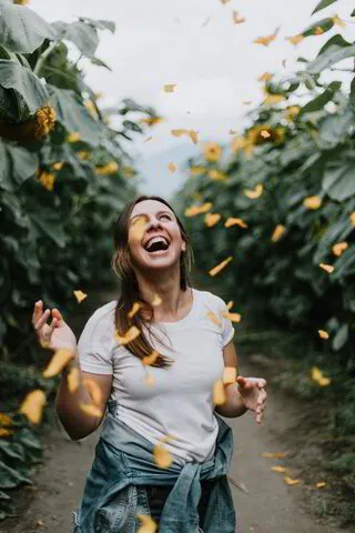 Woman laughing amidst falling petals in a sunflower garden.