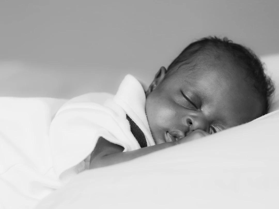 Newborn baby sleeping peacefully on a white pillow in black and white.