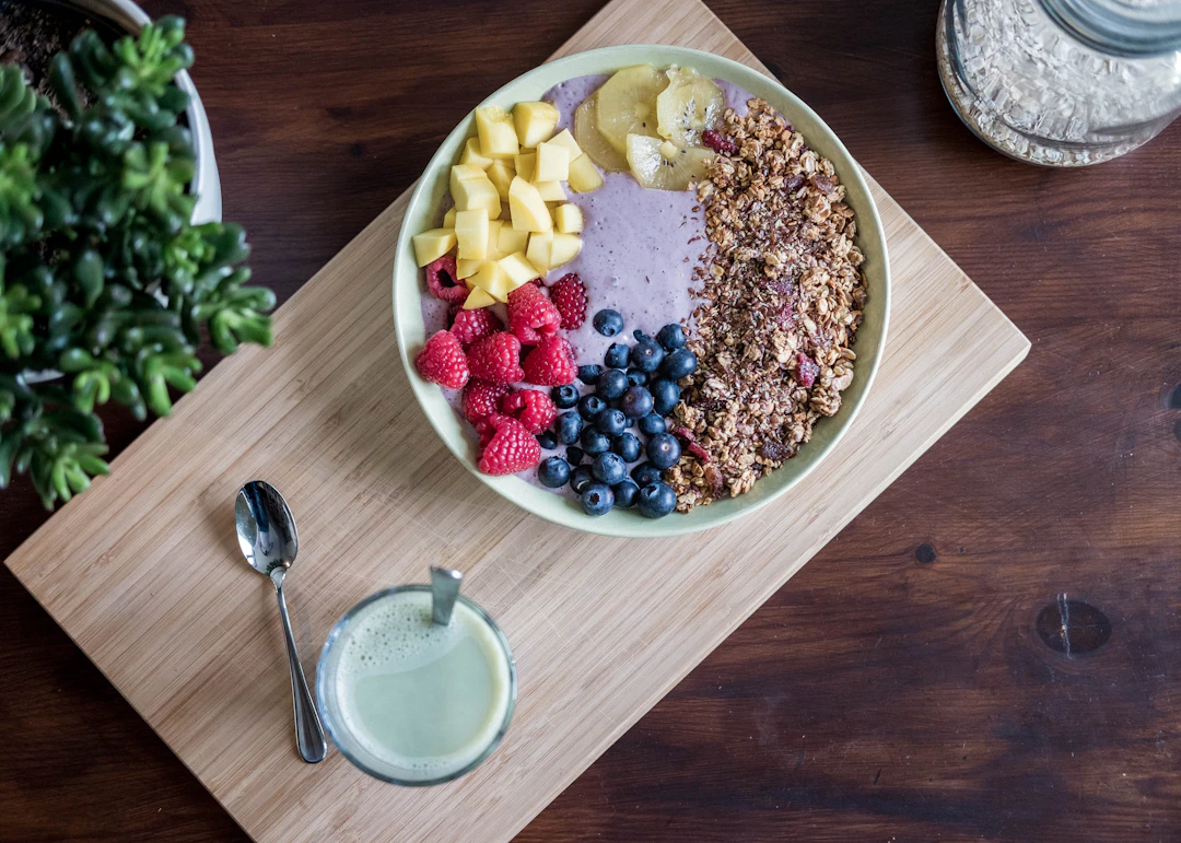 A colorful acai bowl with fresh fruits, granola, and a matcha drink on a wooden board.