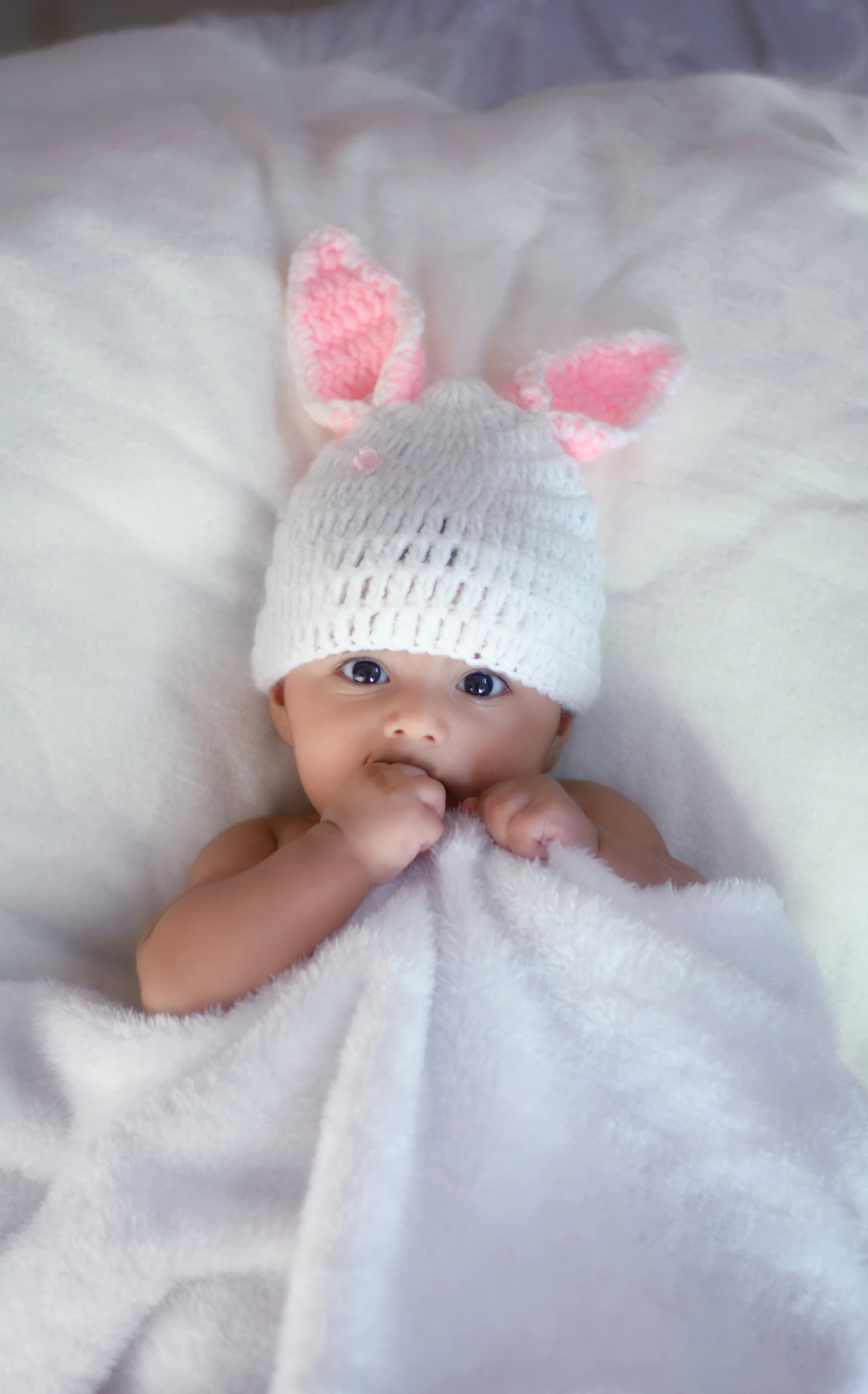Baby wearing a bunny hat lying on a white blanket.