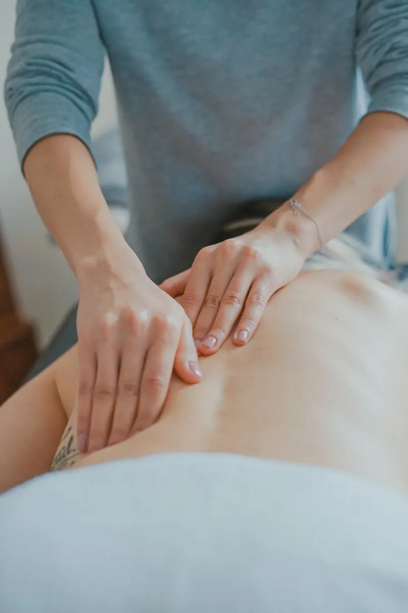 Person receiving a back massage from a therapist's hands in a serene setting.