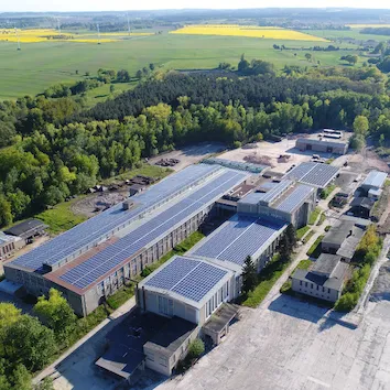Luftaufnahme eines Industriegebiets mit mehreren großen Gebäuden, deren Dächer größtenteils mit Solarpanelen ausgestattet sind.