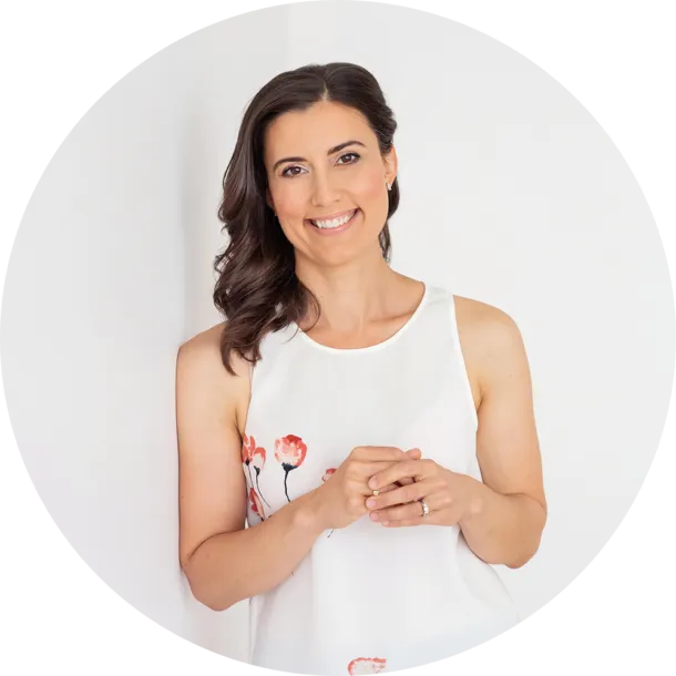 Smiling woman in a white floral dress posing against a white background.