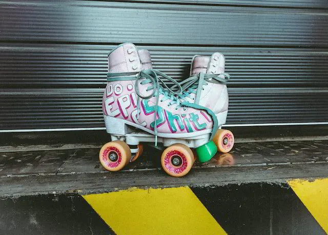 A pair of old school roller skates with pink and blue letters and yellow wheels.