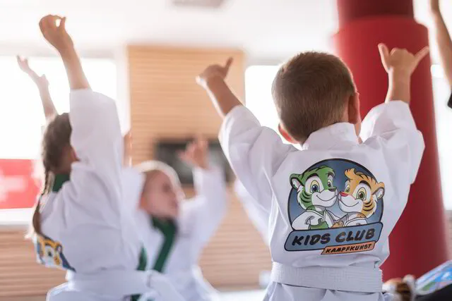 Karate Kinder im Alter von 3-5 Jahren die zusammen im Kreis sitzen und sich freuen und dabei die Hände in die Höhe reißen