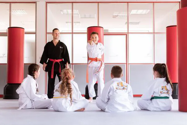 Mitarbeiter bei seiner Arbeit mit Kinder Karate während ein Kind vor der Gruppe etwas Selbstbewusst vormacht