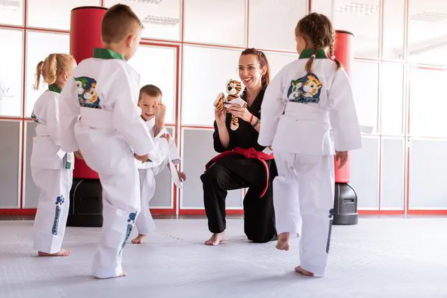 Mitarbeiter übt mit den kleinsten Kids zusammen mit einem Kuscheltier einen Karate Kick. Alle haben Spaß