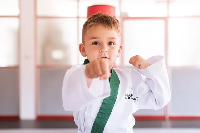 Ein selbstbewusster, starker Karate Junge im Alter von 3-5 Jahren, zeigt seinen starken Faustschlag in die Kamera und wirkt dabei sehr stolz und selbstbewusst, Kinder Karate bei der Kampfkunstschule Geiger