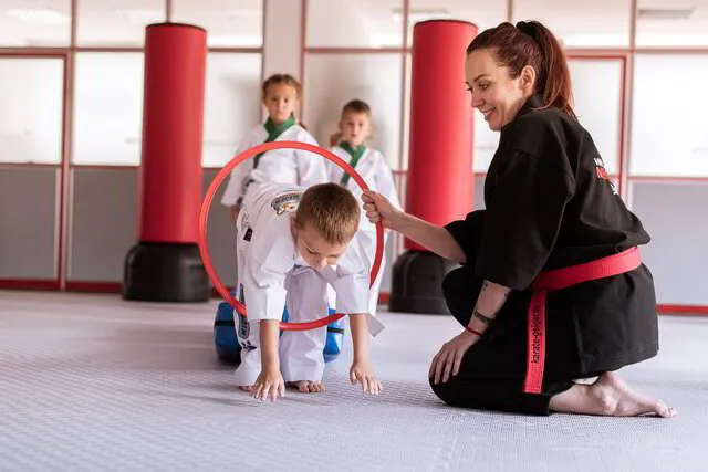 Eine Gruppe von Karate Kids im Alter von 3-5 Jahren stärkt seine motorischen Fähigkeiten im Parcours Training, Die Trainerin bewegt einen Reifen, durch diesen müssen die Kinder hindurchschlüpfend, alle stehen ordentlich an