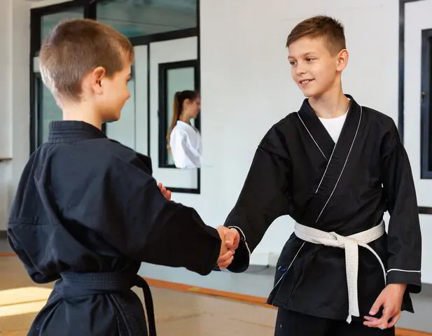 Jugendlicher im schwarzen Karate Anzug gibt anderem Kind die Hand, symbolisiert Respekt bei der Kampfkuntschule Geiger