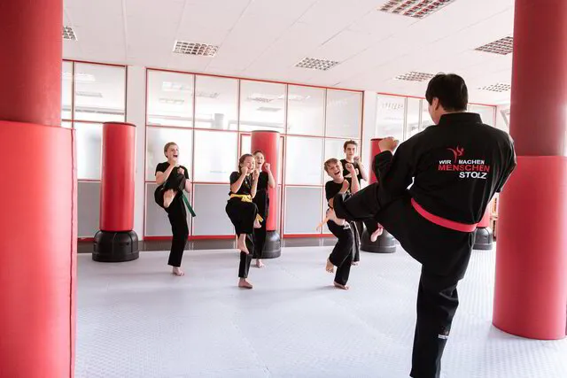 Mitarbeiter zeigt Kindern in der Gruppe einen tollen Karate Kick vor