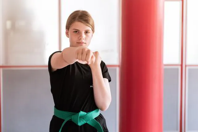 Ein starkes, selbstbewusstes Mädchen macht entschlossen einen Karate Faustschlag in Richtung Kamera, sie hat einen sehr konzentrierten Blick und trägt bereits den grünen Gürtel