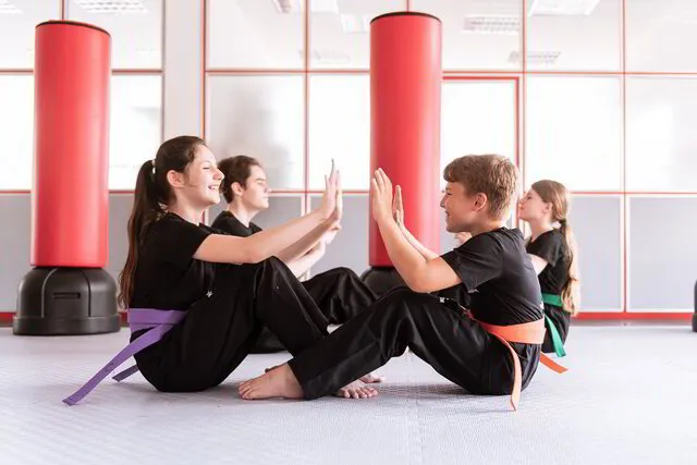 4 Karate Kids stärken im Teamwork mit Situps ihre Bauchmuskeln und gleichzeitig ihre sozial Kompetenz, sie sind an den Füßen zusammen eingehakt und geben sich bei jedem hochkommen einen doppel High Five