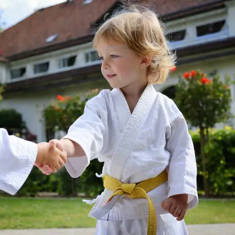Kind im Kinder Karate Training gibt anderem Kind die Hand, beide tragen einen gelben gürtel, symbolisiert Respekt bei der Kampfkuntschule Geiger