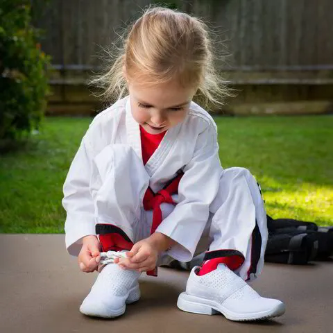 Ein Kind im Karate Anzug mit rotem Gürtel bei Karate Geiger, das konzentriert seine Schuhe bindet
