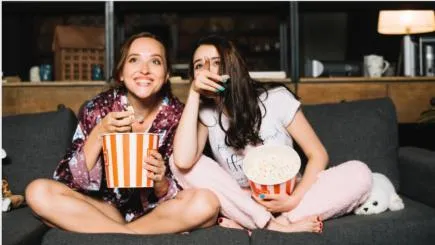 Zwei junge Frauen die Fernsehn und Popcorn essen. 