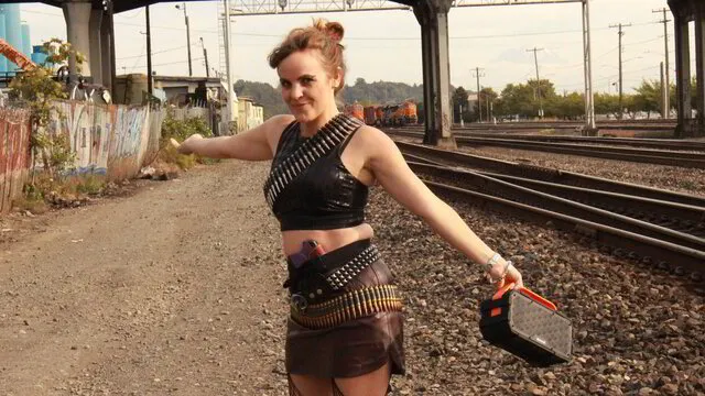 Still shot from Abby London's 'Off The Grid' music video, featuring the political anti-pop singer beside a stretch of railroad track, reflecting her thematic focus on disconnecting from technology and society.