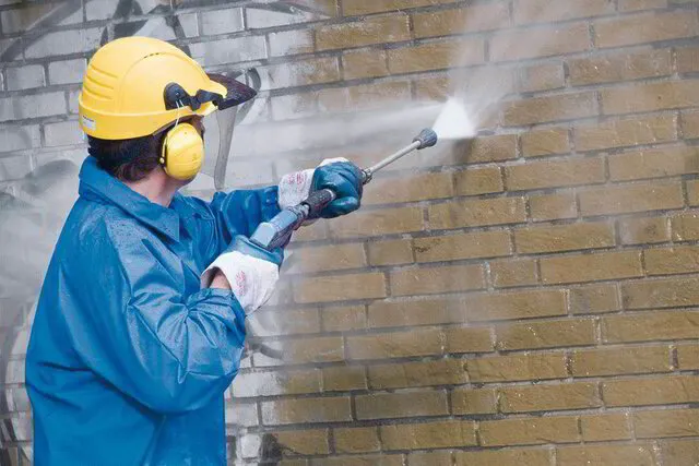 Man pressure washing and removing graffiti from a brick wall