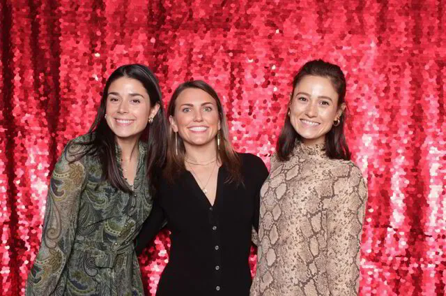 three women standing in front of a premium photo booth backdrop