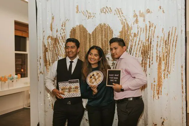 three people posing with signs infront of a photo booth