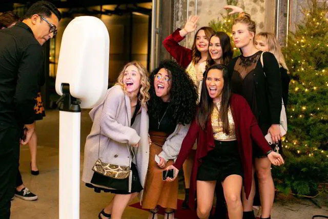 seven ladies posing infront of a digital drop off photo booth for holiday party